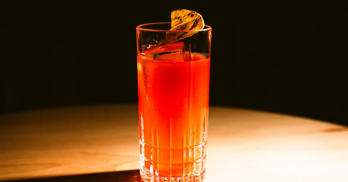 A vibrant Balinese cocktail with a citrus garnish on a wooden table, beautifully lit to highlight its vivid colour.