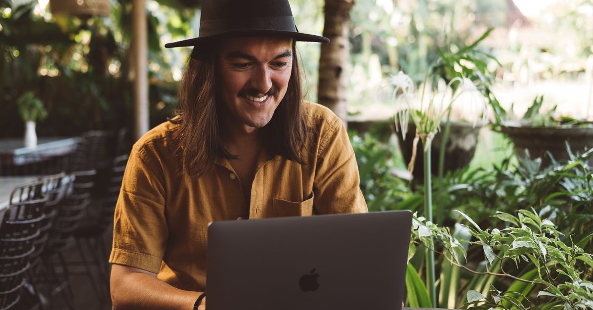 A smiling digital nomad working on a laptop in a lush Balinese garden, evoking remote work in Bali