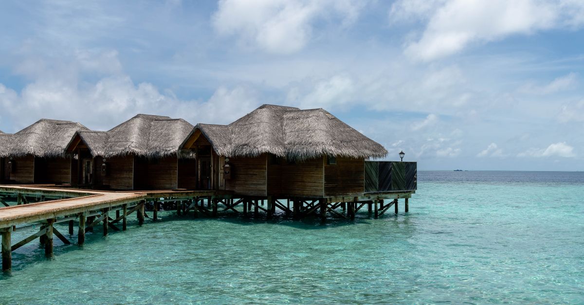 Overwater bungalows with thatched roofs on a turquoise ocean, under a clear blue sky in the Maldives.