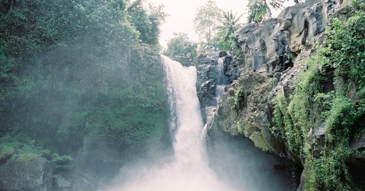 Waterfall cascading down rocky cliffs surrounded by lush green jungle in Bali.