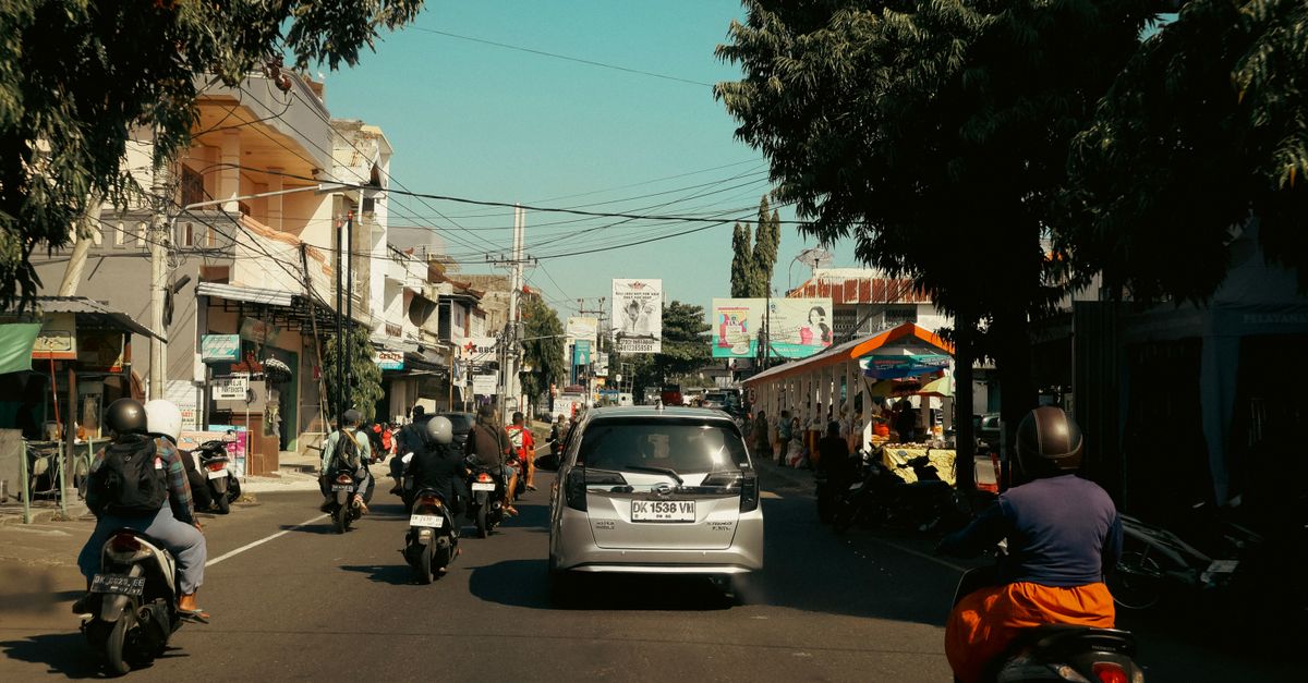 Busy urban road in Bali, Indonesia with motorcycles and cars under a sunny sky.