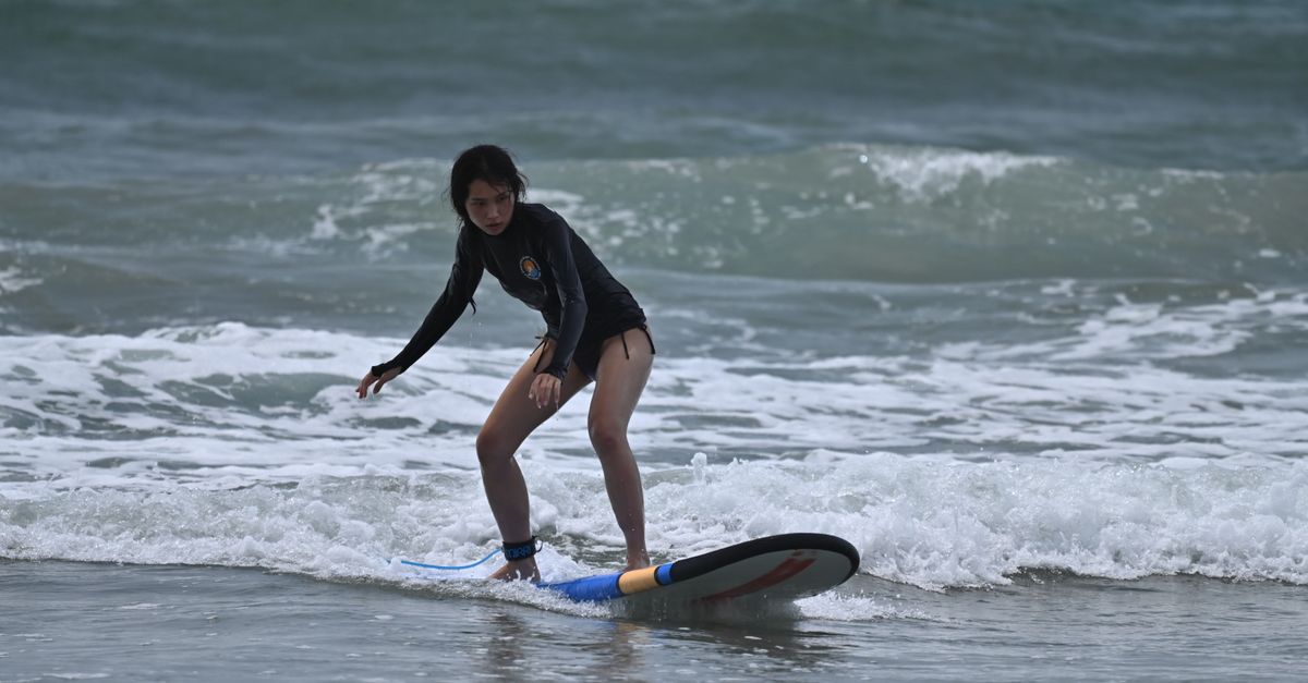 A young woman catching a small white-water wave on a surfboard at a Bali beach