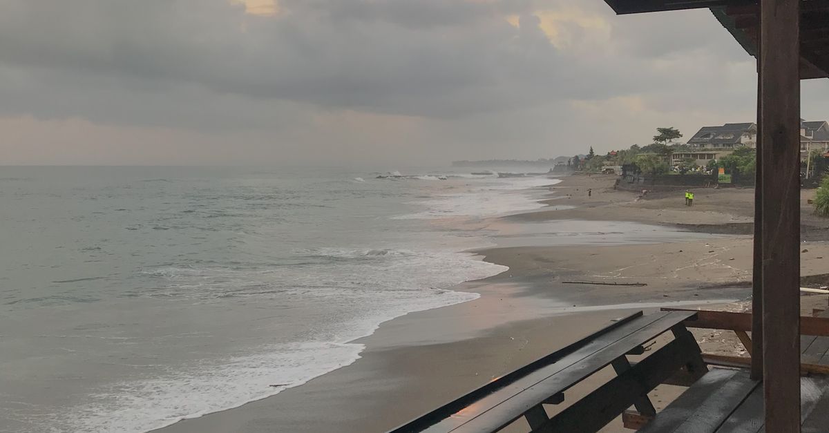 A quiet empty wooden terrace looking out over a Bali beach at sunset, with no one in the frame